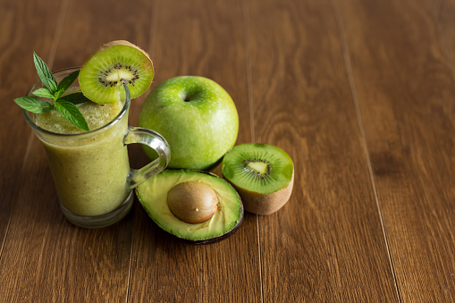 Blended green smoothie with fresh avocado, kiwi and green apple on brown wooden table