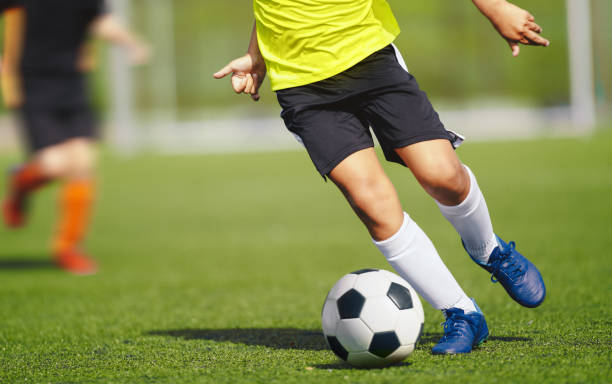 istock Young boy in yellow soccer jersey uniform running after ball on training pitch. Kid improving dribbling skills on practice session 1285932209