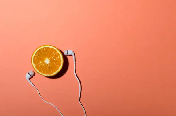 Vertical image.Half of juicy orange and white earphones on the bright background.Concept of summer fun and music