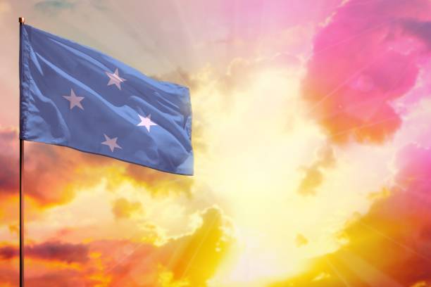 istock Fluttering Micronesia flag in top left corner mockup with the space for your text on beautiful colorful sunset or sunrise background. 1285932430