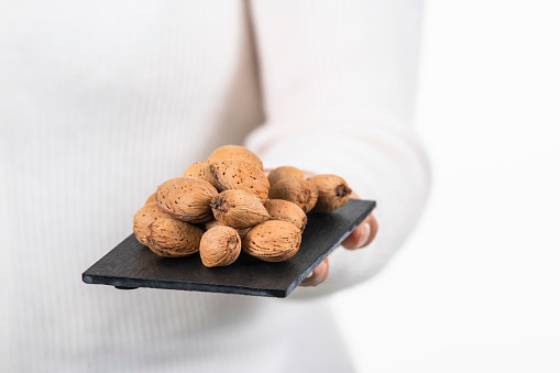 Selective focus of a slate tray with raw almonds with its shell on an out of focus background. Healthy food and natural ingredients concept.