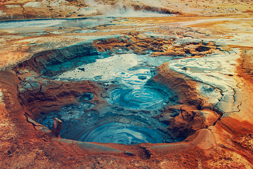 Mudpots in the geothermal area Hverir, Iceland. The area around the boiling mud is multicolored and cracked.
