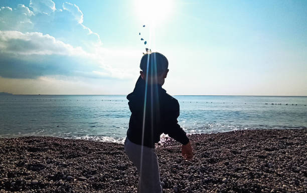 menino jogando pedras no mar - throwing stone little boys child - fotografias e filmes do acervo