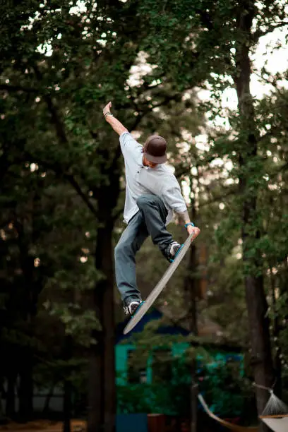 Active man with skateboard simulator jumps masterfully on trampoline against the backdrop of green trees