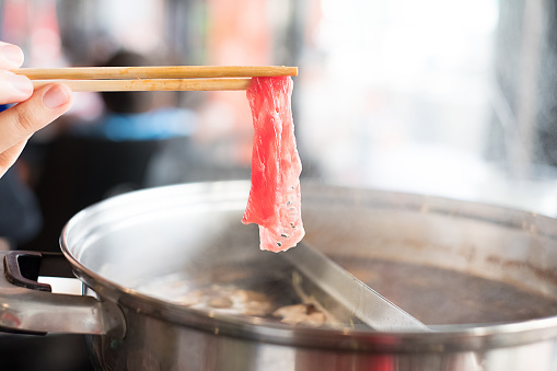 Hand holding chopsticks with beef in Shabu Shabu and Sukiyaki hot pot