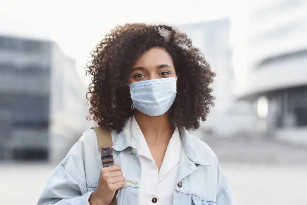 Masked african-american woman on a city street. Teenage girl patient, copy space. Epidemic, pandemic, corona virus protection, healthy lifestyle, people concept