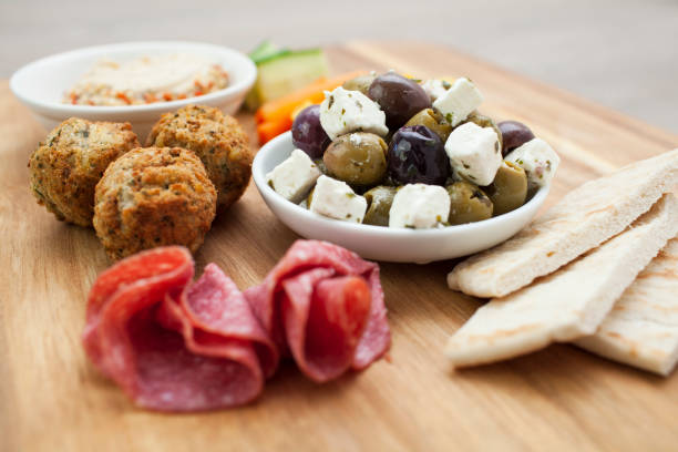 Meze platter of mixed olives and feta, falafel, salami, hummus, and pita bread with sticks of cucumber and carrot on a wooden board Mediterranean inspired sharing platter or appetizer party idea meze stock pictures, royalty-free photos & images