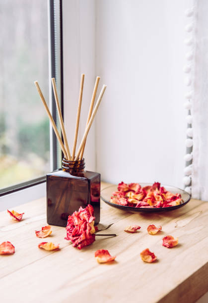 istock Brown glass bottle container with wood stick diffusers on home wooden window sill with beautiful dry pink rose petals for decoration. Minimalist air freshener concept. 1285941177