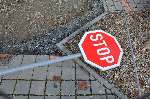 overturned traffic sign after a traffic accident. lies on the ground on concrete pavement behind a makeshift fence. Signs for car stops must stop at road junctions. accident prevention accident, attack, block, broken, building site, car, city, concrete, crash, damage, demolished, destroy, disaster, fell, fence, grass, ground, investigation, kill, lawn, makeshift, metal, nature, oops, path, pedestrian, pole, police, polygonal, post, preference, rebut, red, refute, road, safety, sidewalk, sign, stop, street, temporary, terrorism, track, upright, uprooted, urban, vandalism, vehicle, wind, wreck, heptathlon stock pictures, royalty-free photos & images