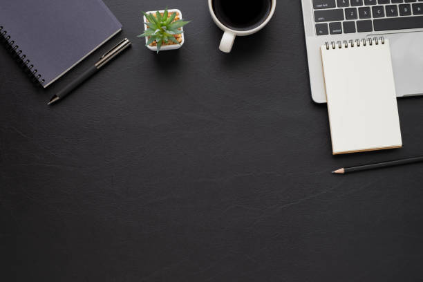istock Top view above of Black leather office desk table with keyboard, notebook and coffee cup with equipment other office supplies. Business and finance concept. Workplace, Flat lay with blank copy space. 1285942079