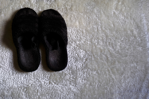Black fluffy slippers on fluffy white carpet in the bedroom. Top view. Home interior. Home clothing, and footwear