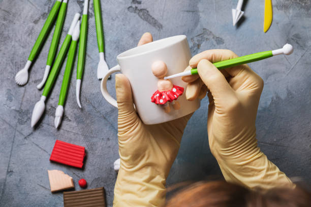 The master sculpts a human figurine on a white ceramic mug made of polymer clay, top view The master sculpts a human figurine on a white ceramic mug made of polymer clay, top view polymer clay stock pictures, royalty-free photos & images