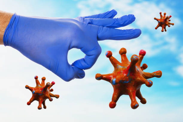 A hand in a medical glove clicks its fingers on a coronavirus against the background of the sky. Concept on the victory over the pandemic covid-19 stock photo