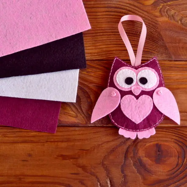 Photo of Funny maroon felt owl with a pink heart. Christmas presents on wooden background. Cheap Christmas tree decorations diy ornaments