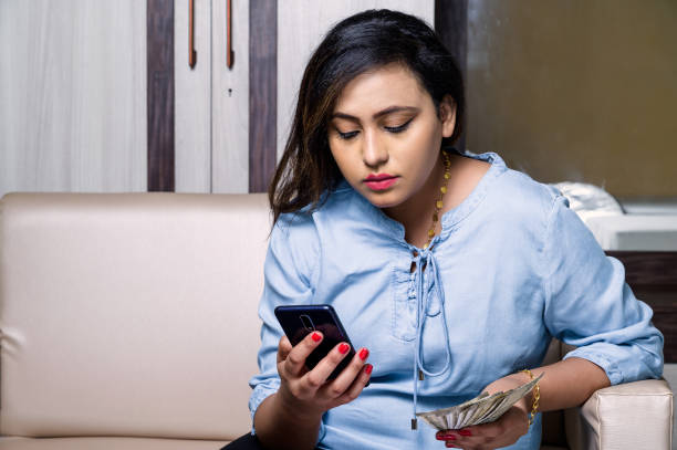istock Young woman sitting on sofa and paying bills with her smartphone. 1285947899