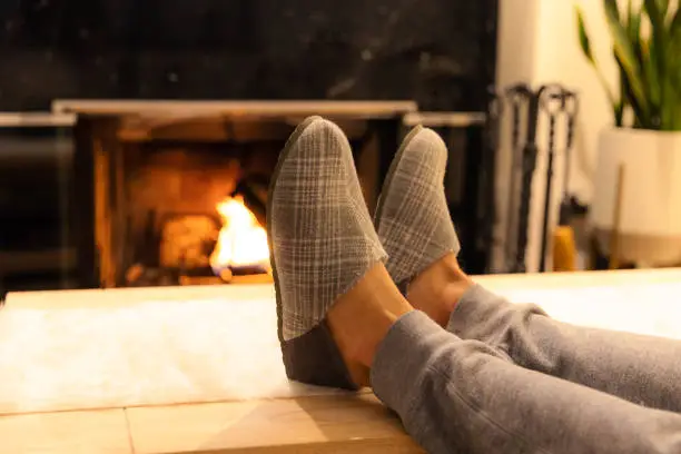 Man in slippers relaxing with his feet up - warm cozy cabin scene with a fireplace in the background.