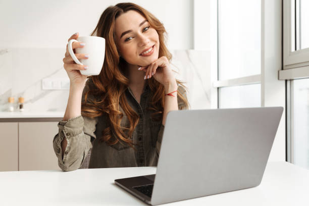 istock Image of happy woman having leisure while sitting at table in kitchen, and working on notebook with cup of tea in hand 1285953606