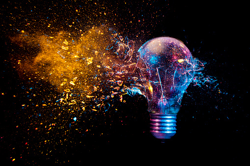 explosion of a traditional electric bulb. shot taken in high speed, at the exact moment of impact. Colored lights and black background. concept of creativity and fragility.