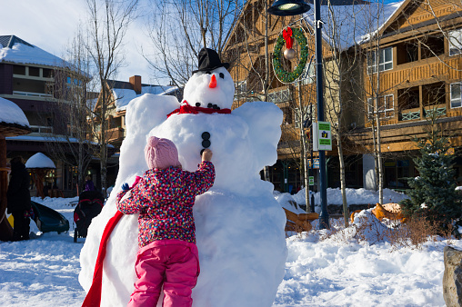 Girl working on a snowman in Whistler village. Top ski resort in North America. Canadian travel destinations for winter.