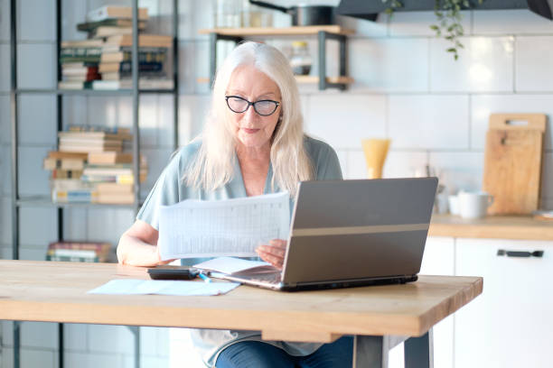 istock Senior woman using laptop for web surfing in her kitchen 1285959841