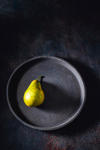 Conference pear on a dark black plate and moody low key gray background copy space
