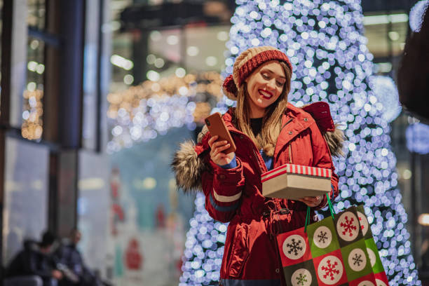 istock Young woman in a shopping holding presents and using mobile phone 1285962430