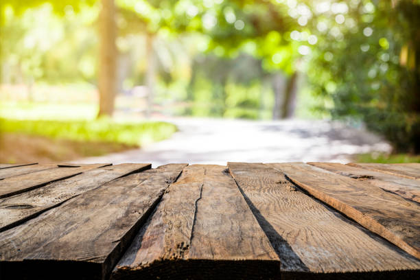 istock Backgrounds: empty rustic wooden table with defocused footpath and yellowish lush foliage at background 1285962678