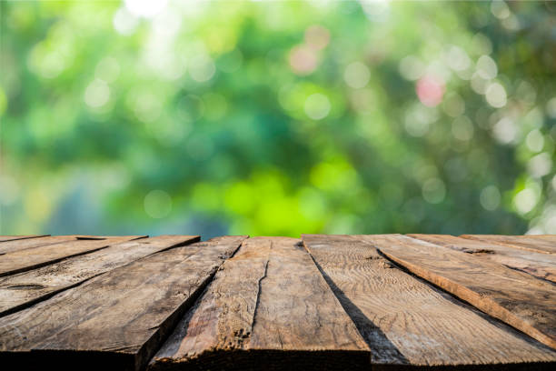 Empty rustic wooden table with defocused green lush foliage at background. Ideal for product display on top of the table. Predominant color are green and brown. High resolution 42Mp studio digital capture taken with SONY A7rII and Zeiss Batis 40mm F2.0 CF lens
