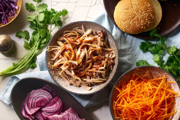 Flat lay with shredded pulled pork, barbecue sauce, pickled vegetables and buns. Cooking burger with slow roasted pork