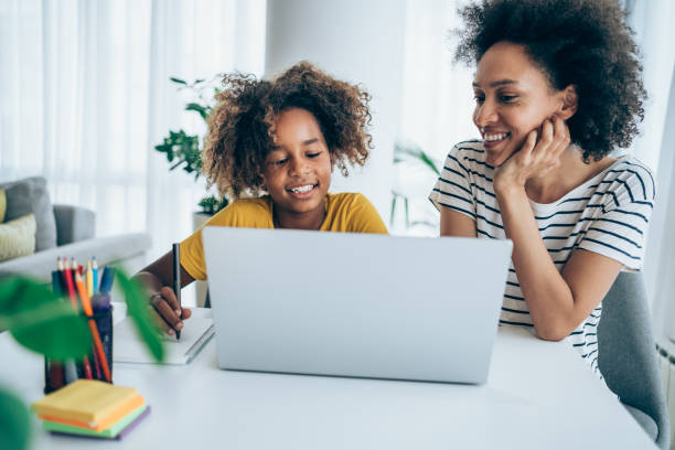 Mother and daughter studying online at home. Mother helps her daughter in distance education classes. African-American mother and her daughter using laptop at home together. Homeschooling and distance learning concept. home schooling homework computer learning stock pictures, royalty-free photos & images