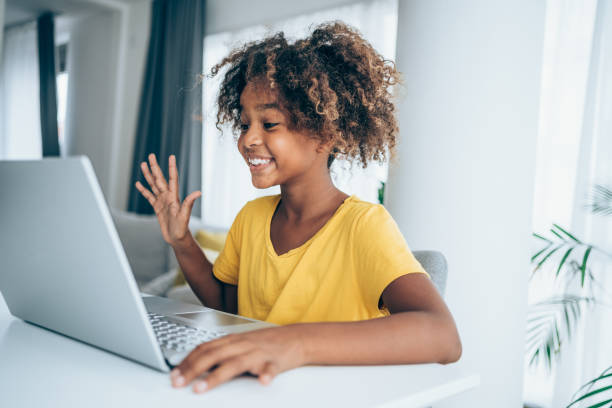 Cheerful girl having video call at home. Cute african-american child having video call at home. Shot of a little girl using a laptop for video conference. Young student watching lesson online and studying from home. Girl using laptop for online lessons. kid waves stock pictures, royalty-free photos & images