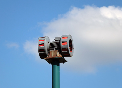 vieja sirena de advertencia mecánica en un poste contra un cielo azul nublado photo
