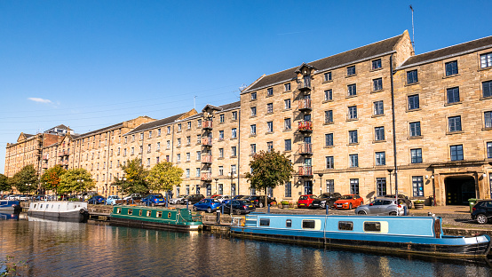Narrowboats and cars outside the historic buildings at Spiers Wharf near Cowcaddens in Glasgow on a sunny day.