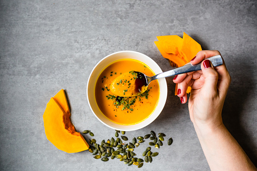 Woman eating homemade, fresh and good looking  pumpkin soup in white bowl on beautiful background