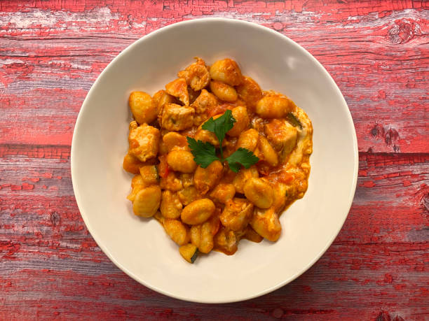 istock Oven baked gnocchi with chicken strips, tomato sauce, vegetables and cheese on red painted wooden background. Copy space for text. 1285985190