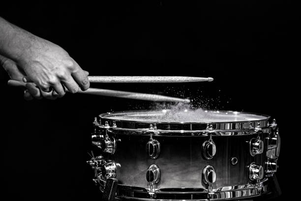 Drum sticks hitting snare drum with splashing water on black background under studio lighting. Black and white. Close up. Drum sticks hitting snare drum with splashing water on black background under studio lighting. Black and white. Photo in motion. snare drum photos stock pictures, royalty-free photos & images