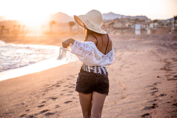 istock A woman in a hat walks at sunset on the beach rear view 1285987978
