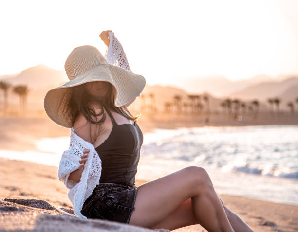 istock Beautiful boho model in a hat poses on the beach in the sun 1285987979