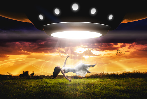 UFO abducts woman. Space ship UFO ray of light in the night sky.