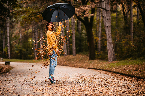 Young cute woman with umbrella in the park, leaves falling from the tress.