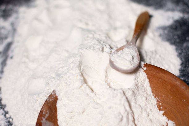 istock White wheat flour in a cup and on the table surface. Wooden spoon. 1285990295