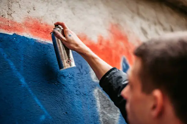 Young male artist painting graffiti on wall outdoors.