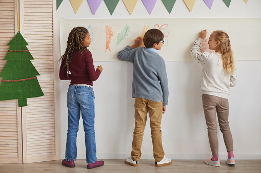 Back view at multi-ethnic group of children drawing on walls while enjoying art class in school, copy space