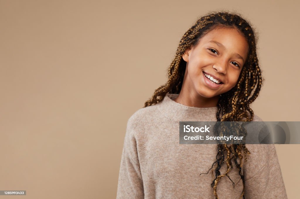 Carefree African-American Girl in Studio Portrait of carefree African-American girl smiling happily at camera while standing against beige background in studio, copy space Child Stock Photo