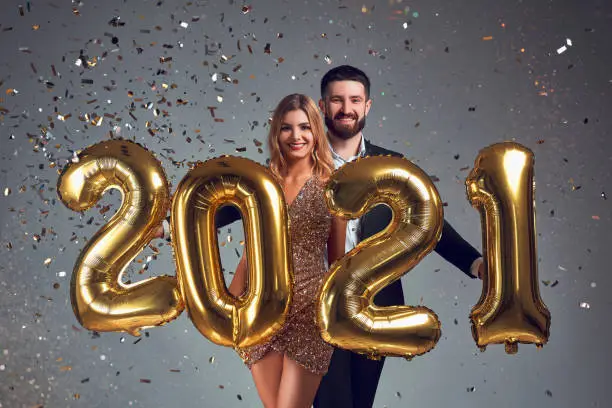 Happy loving couple holds gold 2021 balloons on grey background. New Year celebration. Holidays, festive and party concept.