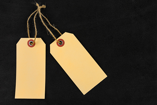 Two blank brown gift tags with a string lying on a black background made of sponge, on the sides.