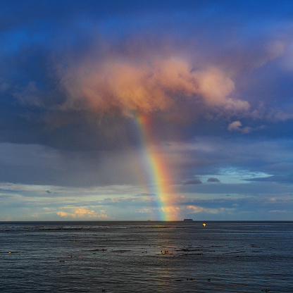 Raincloud with rainbow coming out of in the ocean.