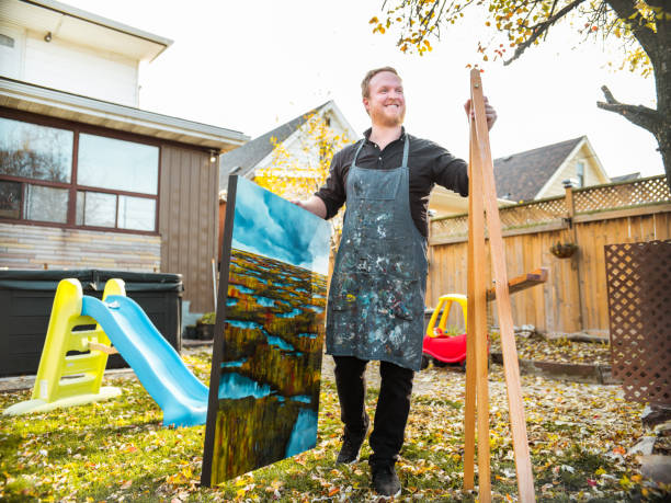 Male artist painting an oil painting in the backyard of his home. Exterior of urban city home in the fall.