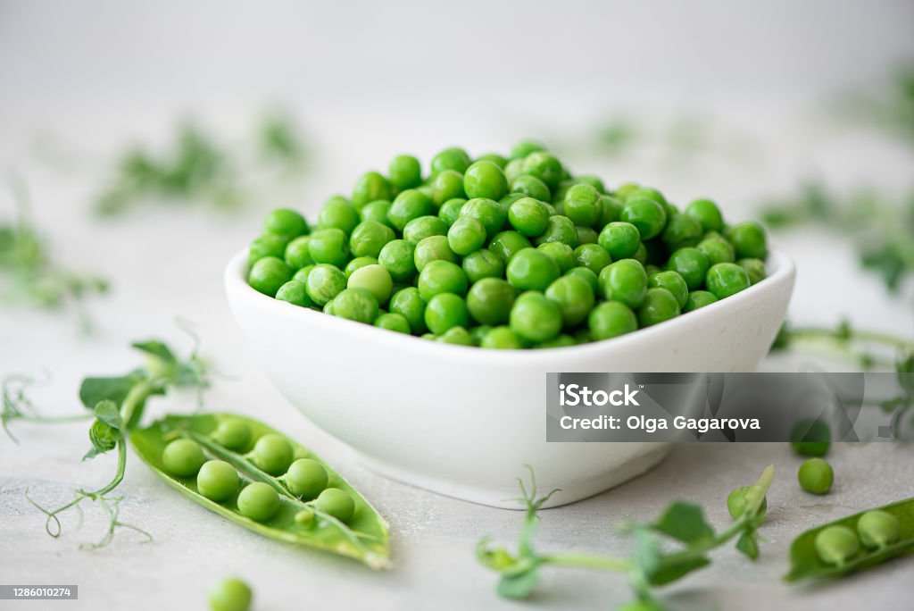 fresh green peas with greens and pea pods fresh green peas with greens and pea pods on a white plate Green Pea Stock Photo