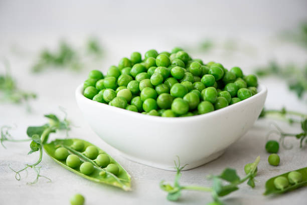fresh green peas with greens and pea pods fresh green peas with greens and pea pods on a white plate green pea photos stock pictures, royalty-free photos & images